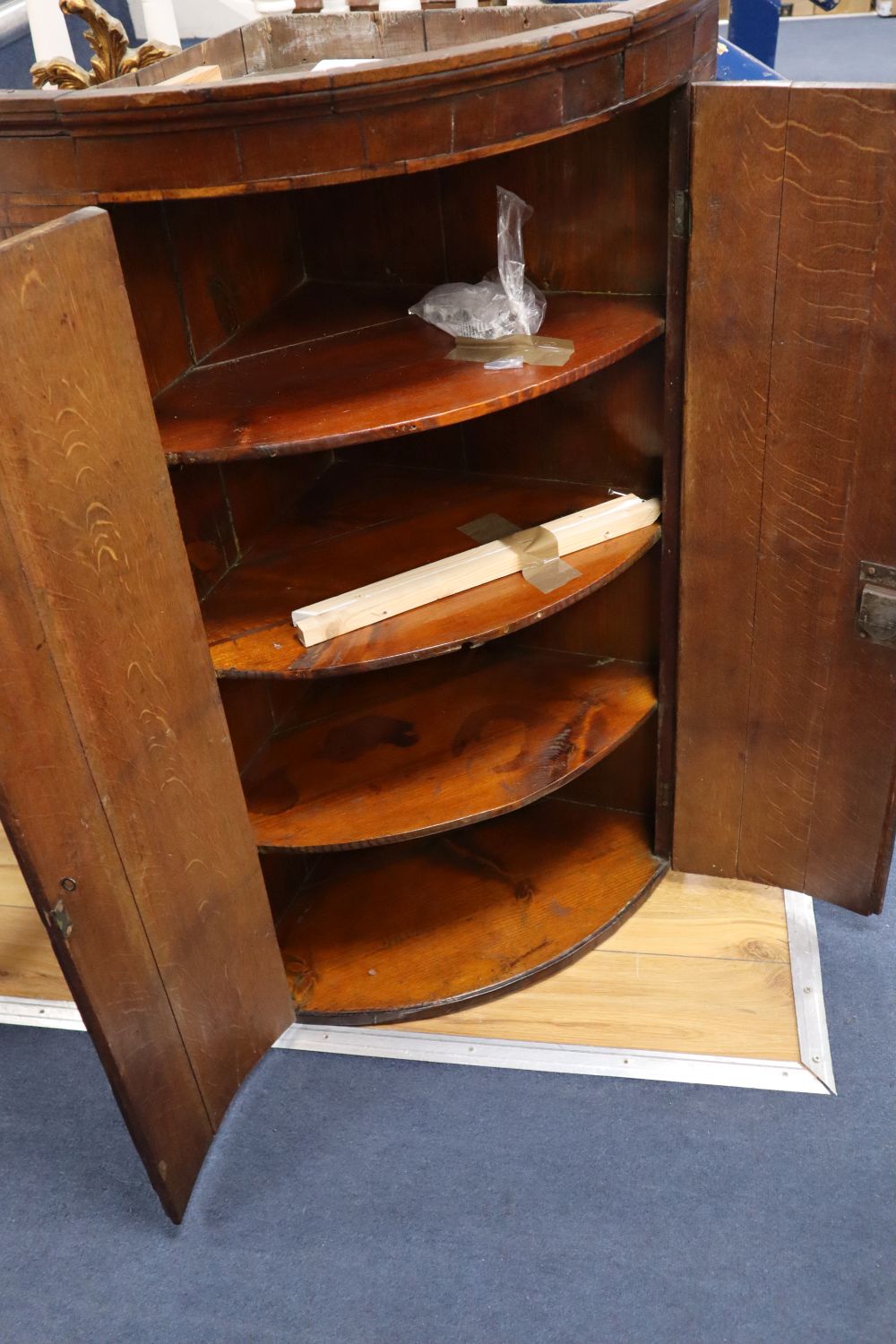 A George III oak bow-fronted hanging corner cupboard, mahogany-banded, width 64cm
